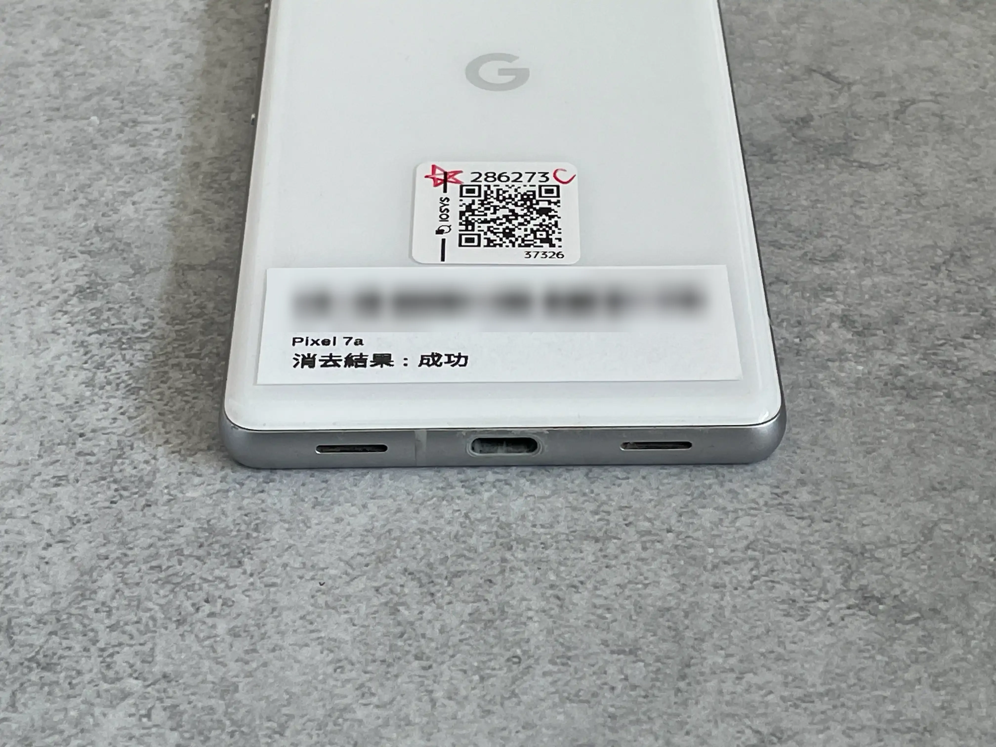 イオシスで買った中古CランクのGoogle Pixel7aの背面。管理シールに「C」の手書きと「消去結果:成功」の印字がある